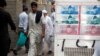 PAKISTAN -- Passersby walk past an advertisement board with photos of Pakistani rupee at a money exchange along a sidewalk in Karachi, Pakistan June 11, 2018.