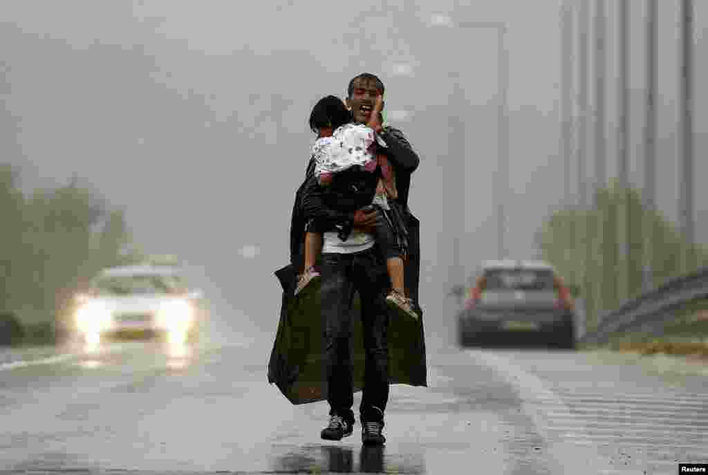 A Syrian refugee screams in frustration as he carries his daughter through a rainstorm toward Greece's border with Macedonia, near the Greek village of Idomeni. (Reuters/Yannis Behrakis)