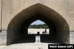 In this 2018 photo, a man walks his bicycle under the 400-year-old Si-o-seh Pol bridge, named for its 33 arches, that now spans a dried up Zayandeh Roud river in Isfahan.