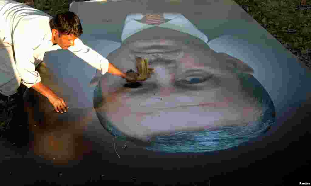 A worker cleans a large picture of Turkish President Recep Tayyip Erdogan as images of the heads of state scheduled to visit Islamabad to attend the 13th Economic Cooperation Organization Summit are hoisted into place. (Reuters/Caren Firouz)