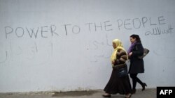 Two women walk past a wall surrounding the burnt and looted house that belonged to the nephew of ousted president in the Tunisdan town of Hammamet.