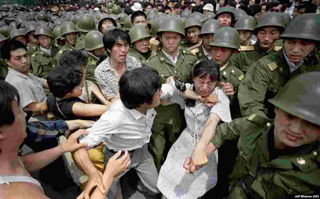 China -- A young woman is caught between civilians and Chinese soldiers, who were trying to remove her from an assembly near the Great Hall of the People in Beijing, June 3, 1989