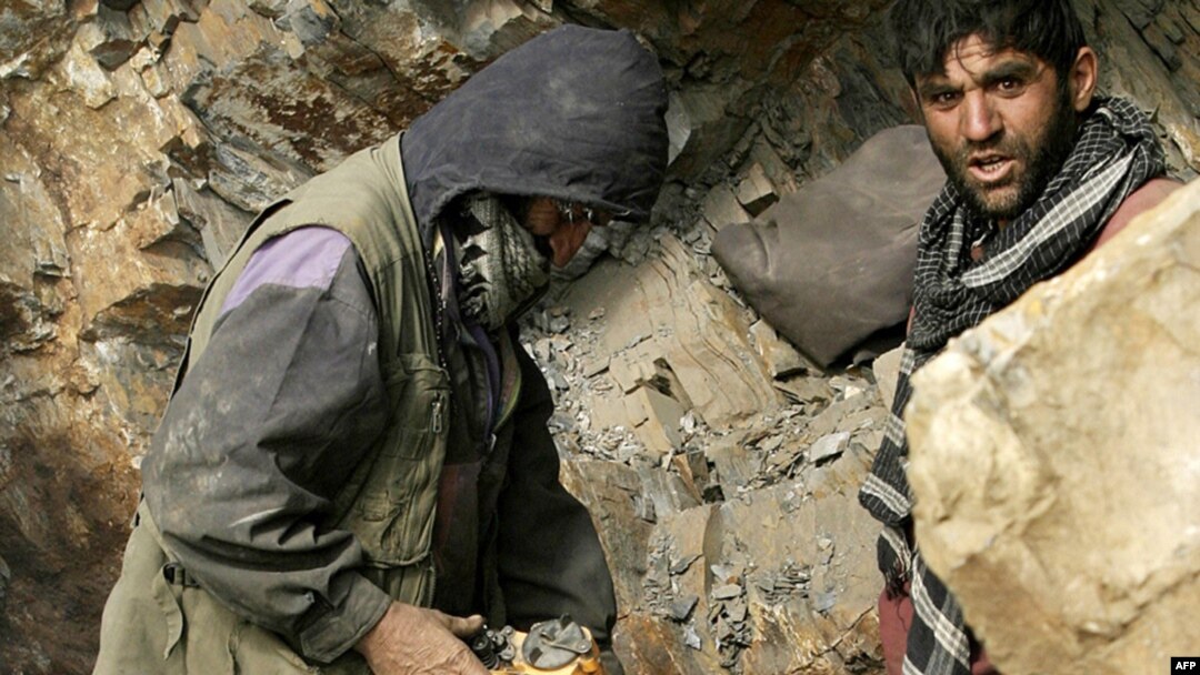 Afghan miners drill into rock in a makeshift emerald mine.