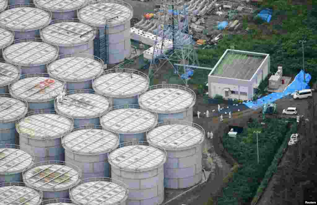 Workers in protective suits and masks stand atop contaminated water storage tanks.