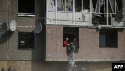Két férfi kitakarítja megrongálódott lakását egy sztrájk után a kelet-ukrán Donbász régióban lévő Kramatorszkban 2022. május 25-én