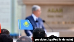 Флаг Казахстана, на заднем фоне выступает президент Казахстана Касым-Жомарт Токаев. Иллюстративное фото