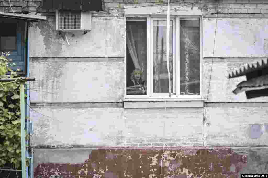 A woman looks out of her apartment window in the city of Lysychansk, a twin city to&nbsp;Syevyerodonetsk just across the Siversky Donets River.