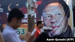 Pakistani men sit near a poster of Pakistan's cricketer-turned-politician and head of the Pakistan Tehreek-e Insaf (Movement for Justice) party Imran Khan, in Islamabad on July 30.