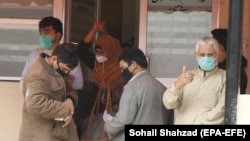 Men wearing protective face masks react outside a building in Islamabad on February 27.