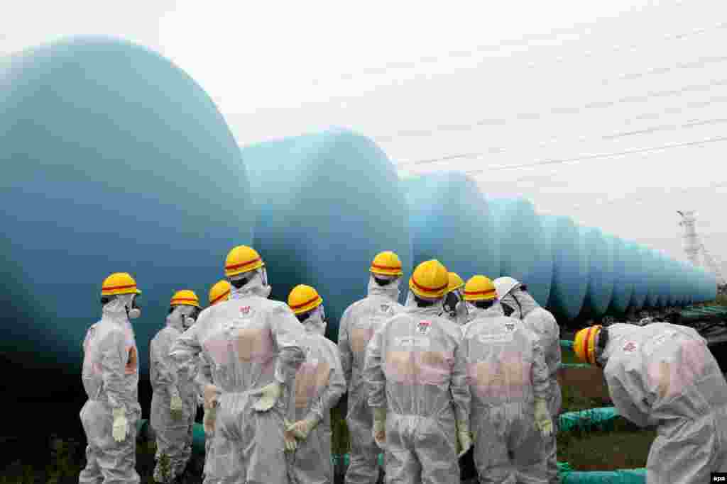 Japan Nuclear Regulation Authority (NRA) employees with protective suits and masks inspect makeshift tanks storing contaminated water at the TEPCO Fukushima Daiichi nuclear power plant.