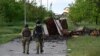 Ukrainian soldiers walk along a path partially blocked by vehicle destroyed in fighting with Russian forces. 