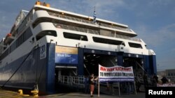 Demonstranti drže transparente ispred privezanog putničkog broda tokom 24-satnog štrajka protiv zakona o reformi rada u luci Pirej u Atini, Grčka, 10. juna 2021.