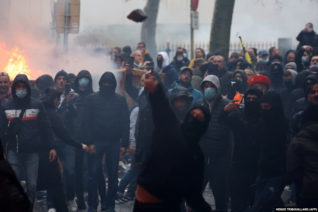 Një protestues duke hedhur gurë në drejtim të njësitit kundër trazirave të policisë, teksa zhvilloheshin përleshje gjatë një demonstrate në Bruksel, Belgjikë, kundër masave për luftimin e COVID-19 në vend, përfshirë pasaportën shëndetësore. (21 nëntor 2021)