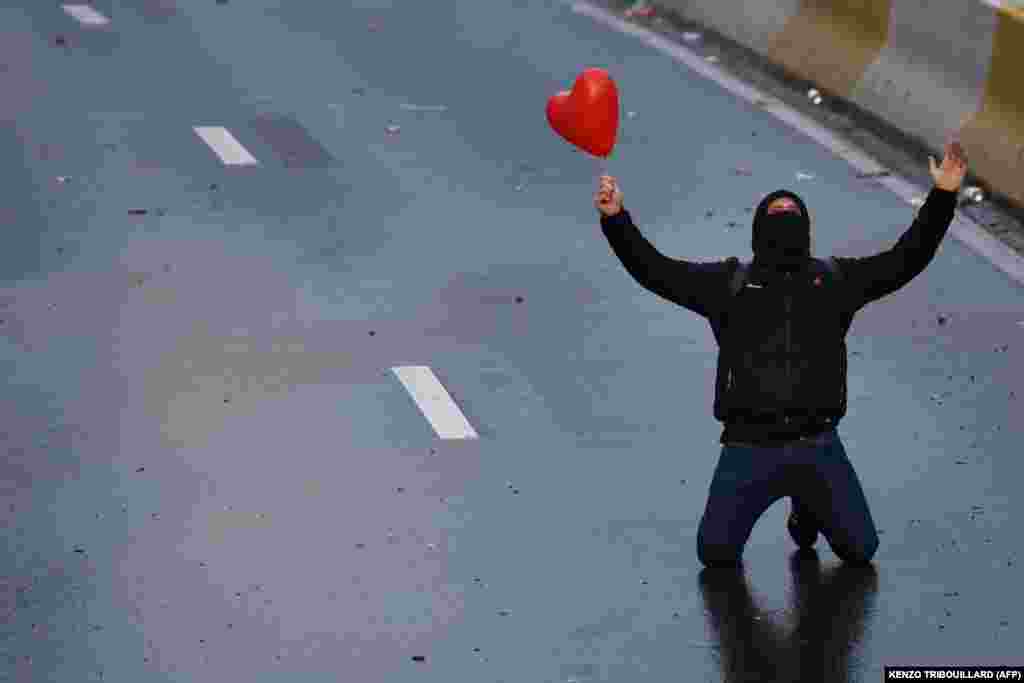 Një protestues, duke mbajtur një balonë me formën e një zemre, i gjunjëzuar në një rrugë në Bruksel, Belgjikë, teksa zhvillohej një protestë kundër masave për luftimin e COVID-19. (21 nëntor)