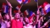 Susținătorii Rassemblement National (RN) flutură steagul Franței în timp ce fosta președintă a partidului, Marine Le Pen, ține un discurs, 30 iunie 2024.