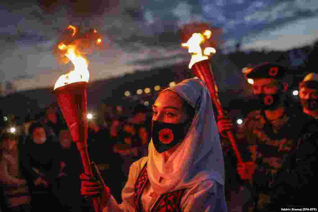 Косовские албанцы в традиционной одежде и военных костюмах держат факелы во время мероприятий, посвященных 23-й годовщине смерти Адема Яшари, командира Освободительной армии Косово (ОАК), в деревне Преказ 7 марта