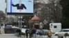 Az elcsatolt Krímben lévő Szevasztopolban emberek sétálnak a februári évértékelő beszédét tartó Vlagyimir Putyin orosz elnököt mutató hatalmas utcai monitor előtt