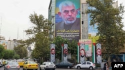 A woman walks past a billboard showing a portrait of Hamas leader Yahya Sinwar next to Palestine Square in Tehran.