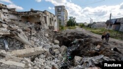 Местные жители стоят рядом с обломками разрушенного здания в Лисичанске, 21 сентября 2022 года
