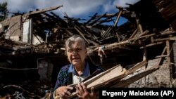 Fűtéshez fát gyűjtő asszony egy lerombolt iskola romjai között Izjum közelében 2022. szeptember 19-én