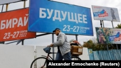 Мужчина проезжает на велосипеде мимо транспарантов, сообщающих о референдуме о присоединении подконтрольных России регионов Украины к РФ, оккупированный Мелитополь , 26 сентября 2022 г.