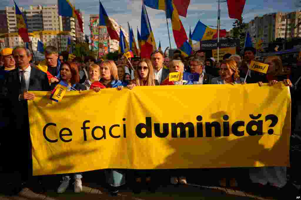 Dorin Recean moldovai miniszterelnök (középen) támogatói mögött, akik egy „Mit csinálsz vasárnap?” feliratú plakátot tartanak a kezükben, a kormányzó Cselekvés és Szolidaritás Párt (PAS) EU-párti tüntetésén, Kisinyovban, Moldovában, 2025. szeptember 26-án, pénteken, a szeptember 28-án tartandó parlamenti választások előtt, amikor a miniszterelnök arra figyelmeztetett, Oroszország milliókat költött rá, hogy „átvegye a hatalmat” a választásokon, szavazatvásárlási programok és kibertámadás segítségével
