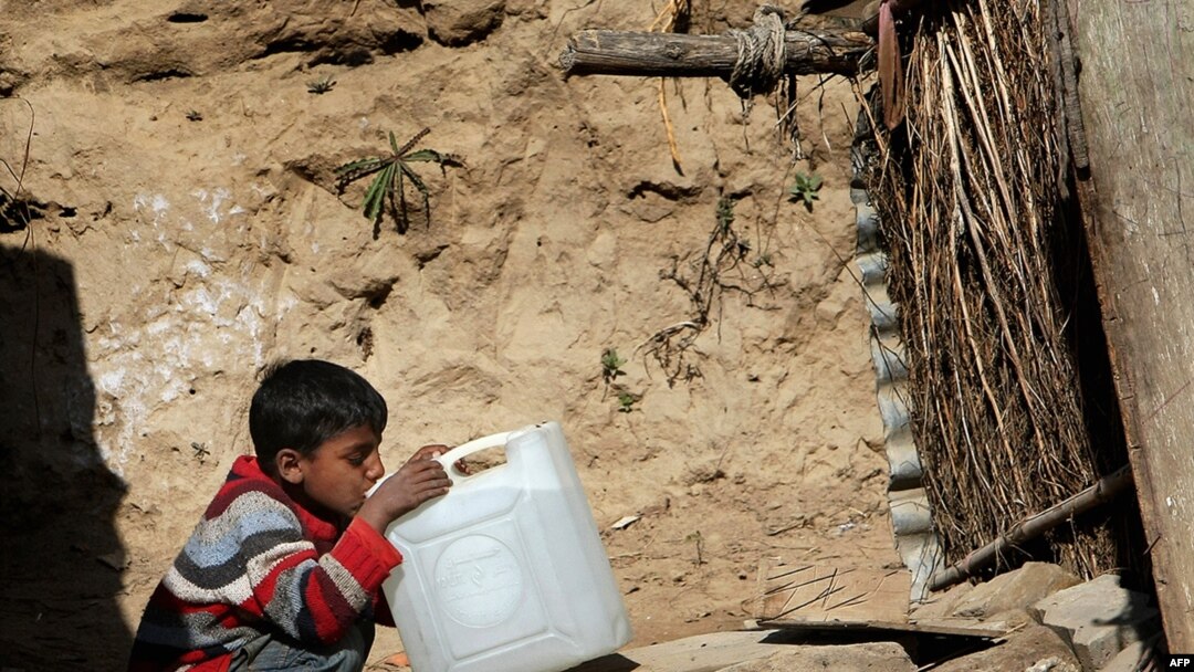 A Pakistani boy drinks water from a gallon container outside his makeshift tent in an Islamabad slum.