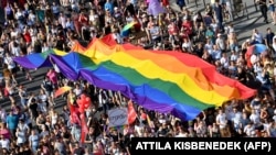 Oameni mărșăluiesc cu steagul curcubeu uriaș dinspre clădirea Parlamentului din centrul Budapestei în timpul paradei LGBT Pride pe 6 iulie 2019.