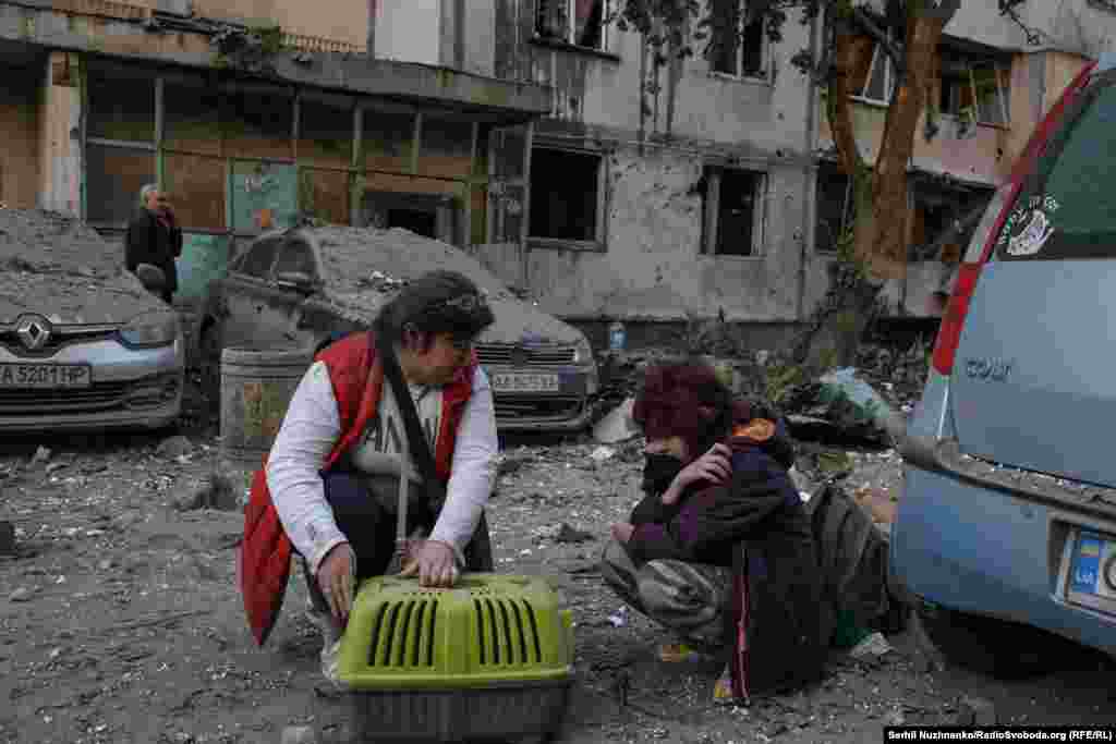A woman hugs her cat close to the site of a missile or drone impact in Kyiv.