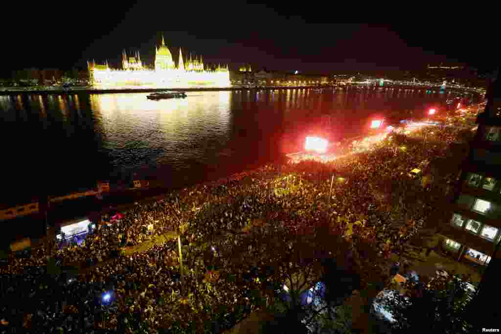 Ljudi okupljeni preko puta zgrade parlamenta na obali Dunava. 