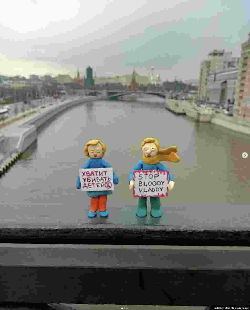 Figurine în fața Kremlinului, pe un pod deasupra râului Moscova. Semnul femeii spune: &bdquo;Opriți uciderea copiilor.&rdquo; Rușii care amplasează în public astfel de figurine de protest ar fi aproape sigur condamnați la ani grei de închisoare dacă ar fi prinși.