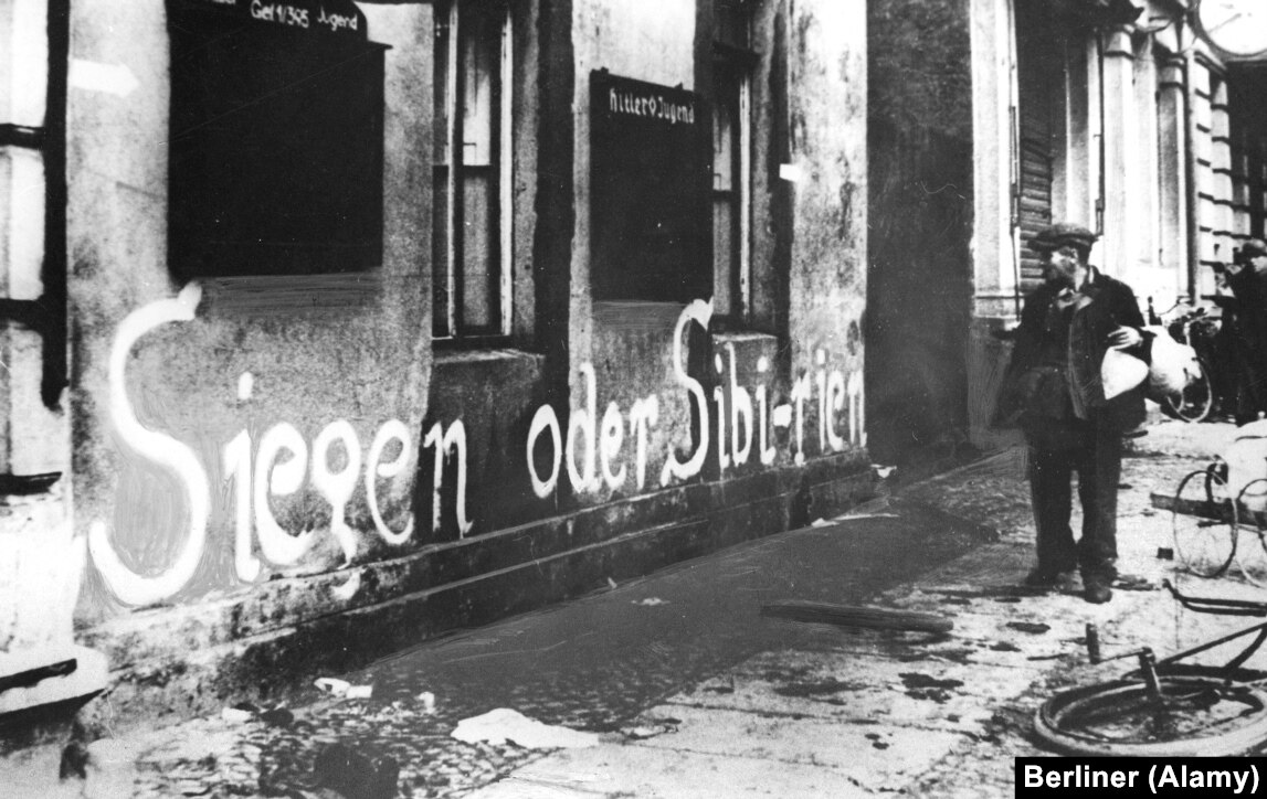 一名德國男子看著「勝利或西伯利亞」這句話畫在建築物上。對於許多留下來的人來說，這句殘酷的格言被證明是正確的。數百萬德國人被蘇聯運往東部，約 357,000 人死於勞改營或秘密警察監獄。  