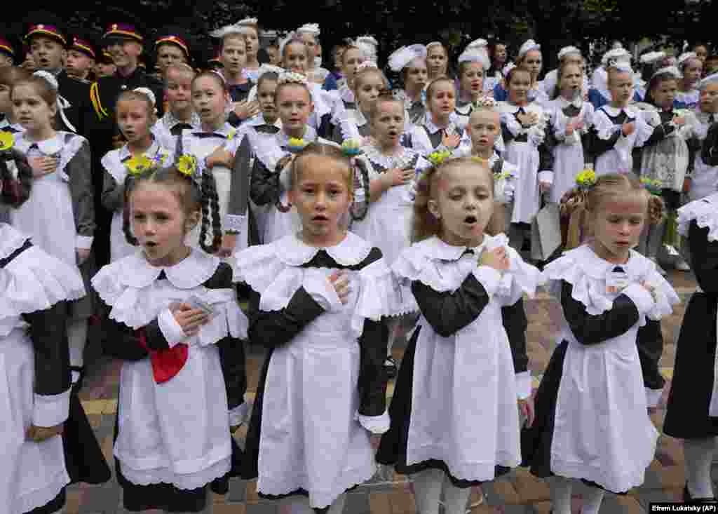 Schoolgirls in traditional uniforms sing Ukraine&#39;s national anthem as they attend a ceremony on the first day in school at a cadet lyceum in Kyiv on September 1.