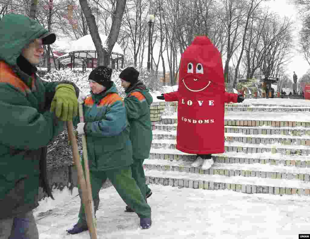 Аніматор в костюмі презерватива біля працівників комунальної служби, які чистять сніг у парку Шевченка. 13-го лютого відзначають Міжнародний день презерватива. Люди мали змогу пройти швидке тестування на ВІЛ в мобільному пункті, безкоштовно отримати контрацептиви і інформацію про ВІЛ-інфекцію. Київ, 13 лютого 2019 року