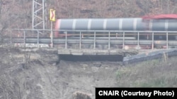 În imagine se văd atât grinda care susține drumul și-l face să reziste la trafic, cât și alunecarea de teren de sub grindă. Alunecarea de teren a scos doar pământul de sub grindă, dar vibrațiile ar putea afecta și fundațiile capetelor pe care se sprijină structura de beton.