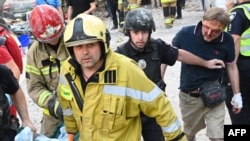 Injured Kyiv resident identified as Yaroslav Bazylevych (right) follows Ukrainian rescue workers carrying the body of one of his daughters, who was killed along with her two sisters and their mother during a missile attack in Lviv on September 4.