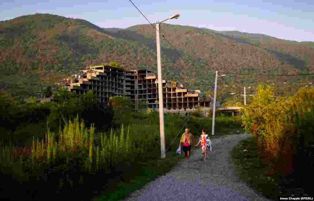 A Russian father and daughter walking to the beach at Gagra. An abandoned building site is in the background.&nbsp;