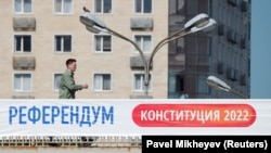 Мужчина идет по мосту возле баннера, информирующего о референдуме в Казахстане. Алматы, 1 июня 2022 года