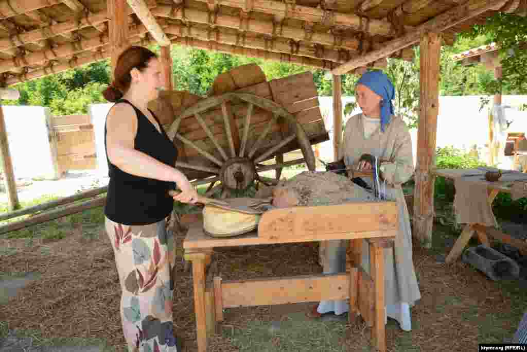 Женщина-реконструктор (справа) рассказывает посетительнице про изготовление украшений из расплавленного стекла по генуэзской технологии