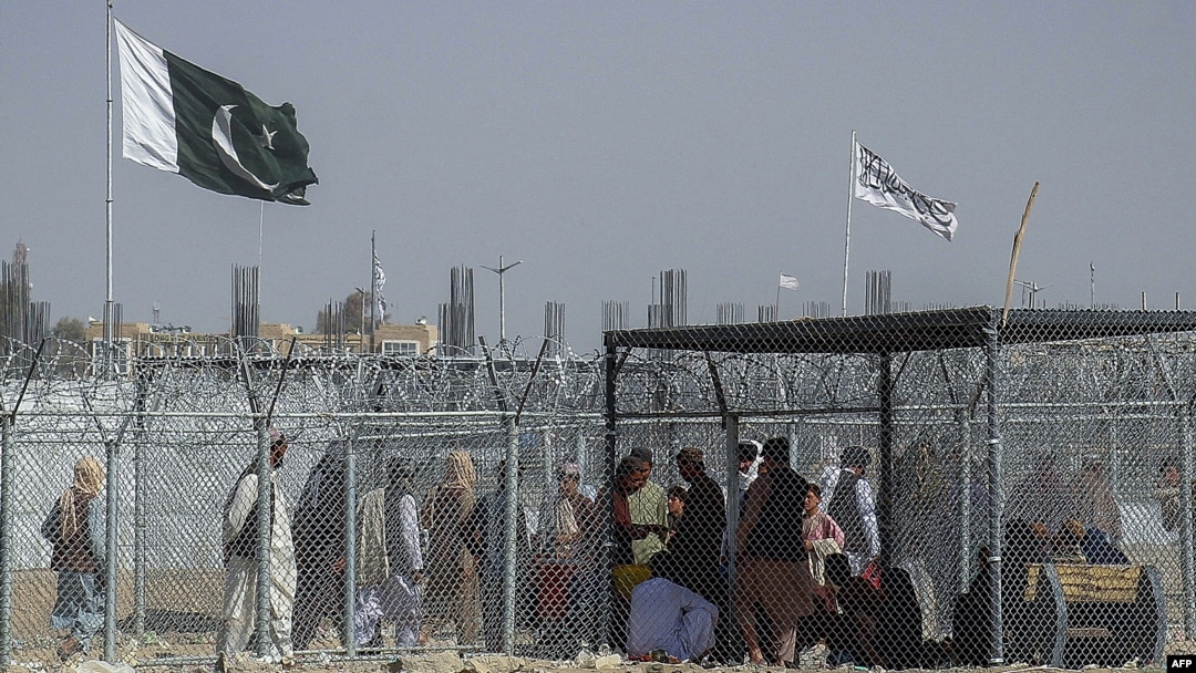 Afghan and Pakistani nationals walk through a security barrier to cross the border as the Pakistani and Taliban flags fly at the Pakistan-Afghanistan border crossing point in Chaman.