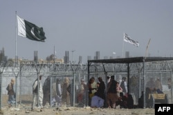 People walk through a security barrier as Pakistani and Taliban flags fly at the Pakistan-Afghanistan border crossing point in Chaman.