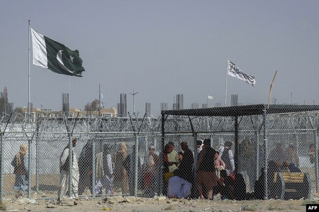 People walk through a security barrier as Pakistani and Taliban flags fly at the Pakistan-Afghanistan border crossing point in Chaman.