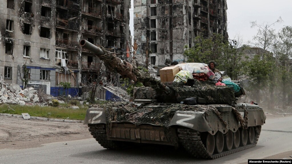 Reseydiñ Ukrainağa basqınşılığı kesirinen qirağan twrğın üylerdiñ qasınan ötip bara jatqan reseyşil küşter äskeri tanki. Popasnaya qalası, Lugansk oblısı, Ukraina, 26 mamır 2022 jıl.