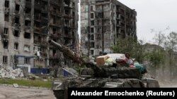 Российский военный на танке с награбленными вещами в Попасной, Луганская область. На заднем плане – разрушенные жилые дома. 26 мая 2022 года