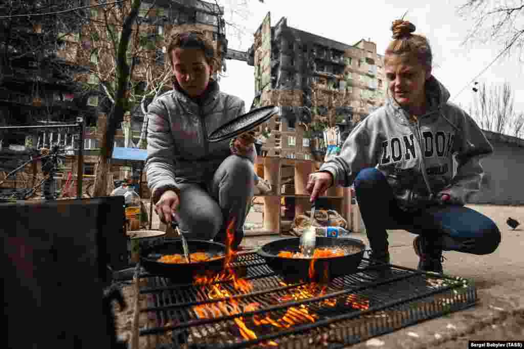 Women cook food over an open fire in Mariupol on April 3. Gas, electricity, and water were cut off as Russian forces pushed into the city.&nbsp;