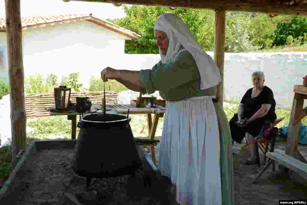 Пожилая женщина-реконструктор показывает технологию изготовления тонких средневековых свечей из воска