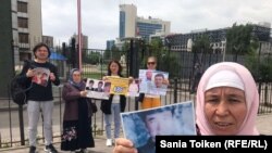 Группа граждан у здания посольства Китая в Казахстане держит плакаты с информацией о задержанных в Китае родственниках. Нур-Султан, 8 июня 2022 года