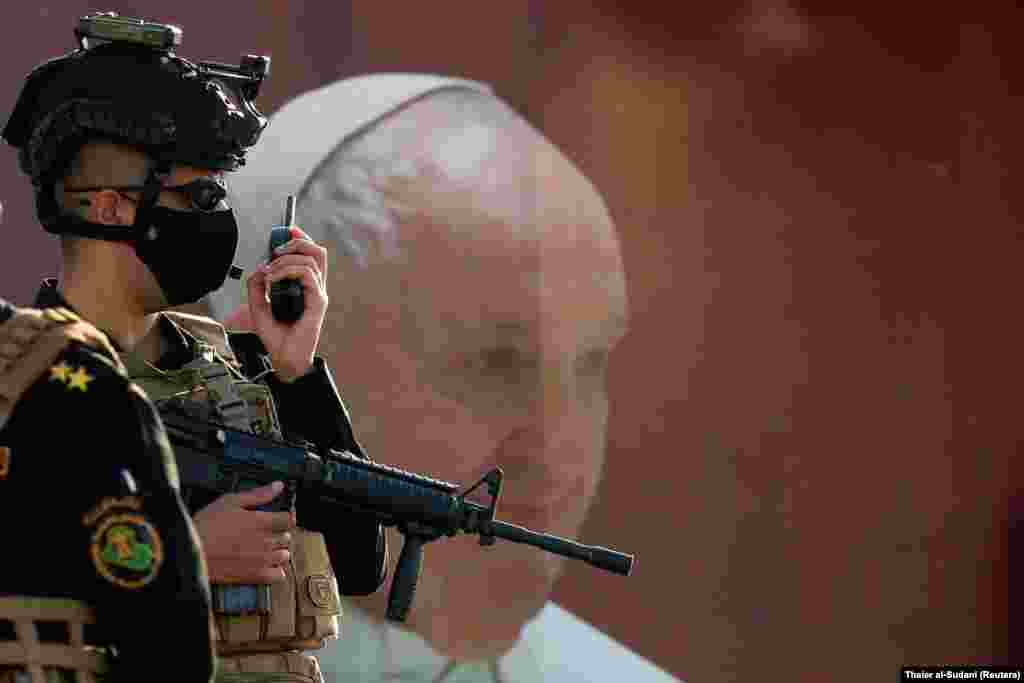 Un membru al forțelor irakiene de securitate lângă un afiș al Papei înaintea sosirii acestuia la Catedrala siro-catolică din Bagdad.