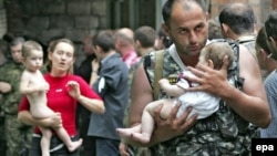 A soldier carries a baby and a woman follows him with another small child after the release of 26 women and their children in Beslan on September 2, 2004.