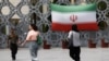 Disa gra iraniane shihen duke kaluar pranë një rruge në Teheran ku është vendosur flamuri i Iranit. 27 prill 2026.